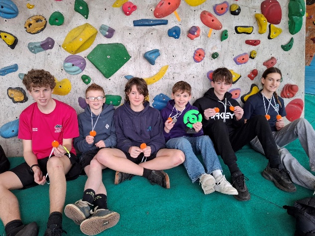 Students holding medals at the bottom of a rock-climbing wall