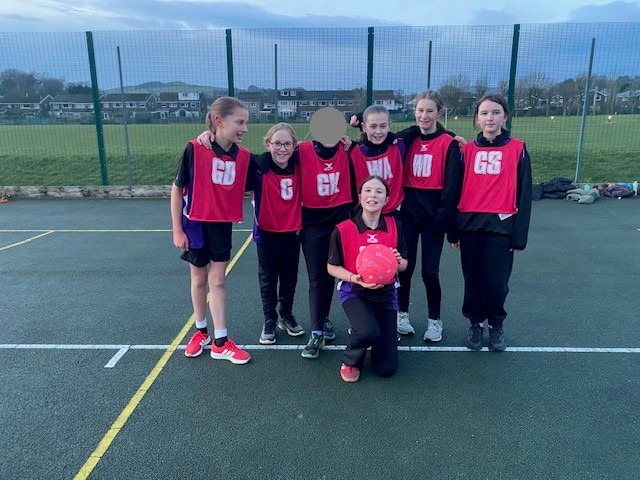 Girls Netball Team in red bibs smiling on the court