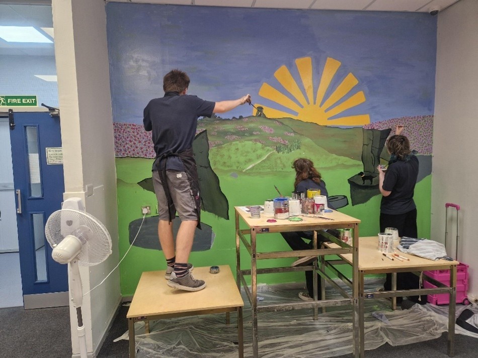 Students painting a mural of hills and sunshine in the Learning Support Centre
