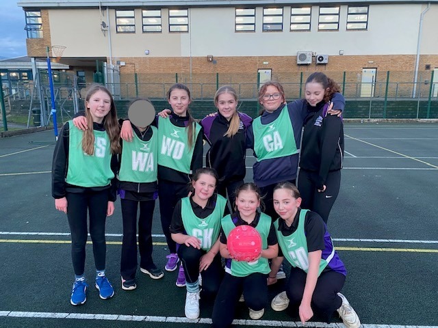 Girls Netball Team in green bibs smiling on the court