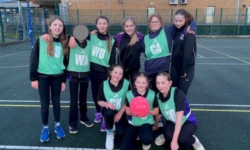 Girls Netball Team in green bibs smiling on the court
