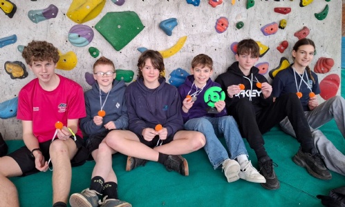 Students holding medals at the bottom of a rock-climbing wall